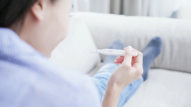 Žena okrenuta leđima drži test za trudnoću u ruci